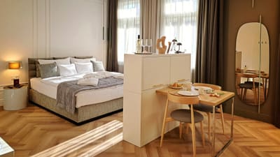 Apartman halszálka parkettával: kárpitozott ágy, reggelizőasztal és álló ovális tükör